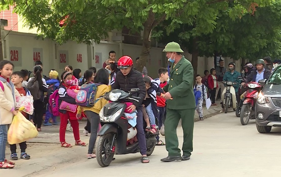 Cựu chiến binh Nguyễn Tiến Nam (mặc quân phục) đang hướng dẫn phân luồng giao thông trước cổng trường.